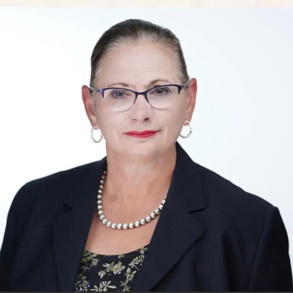 Professional headshot of Anne Gibson wearing glasses and a navy blazer